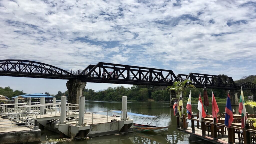 The historic Bridge over the River Kwai in Kanchanaburi, Thailand, spanning the river beside the riverside landing and restaurants.