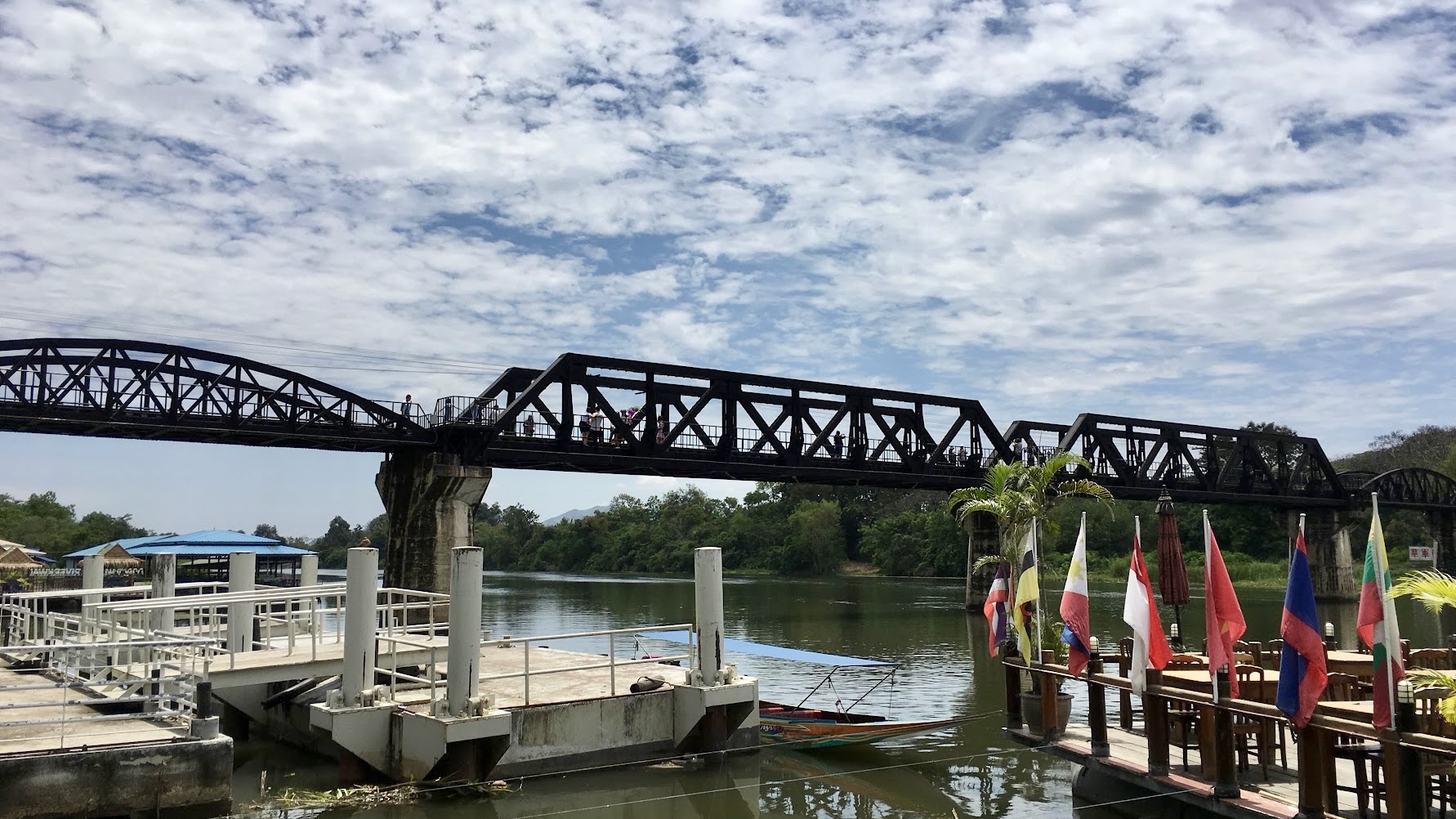 The historic Bridge over the River Kwai in Kanchanaburi, Thailand, spanning the river beside the riverside landing and restaurants.
